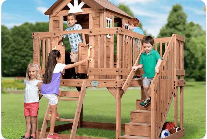 Five children climbing the wooden staircase and deck of a raised cedar clubhouse playhouse with a growth board on the railing