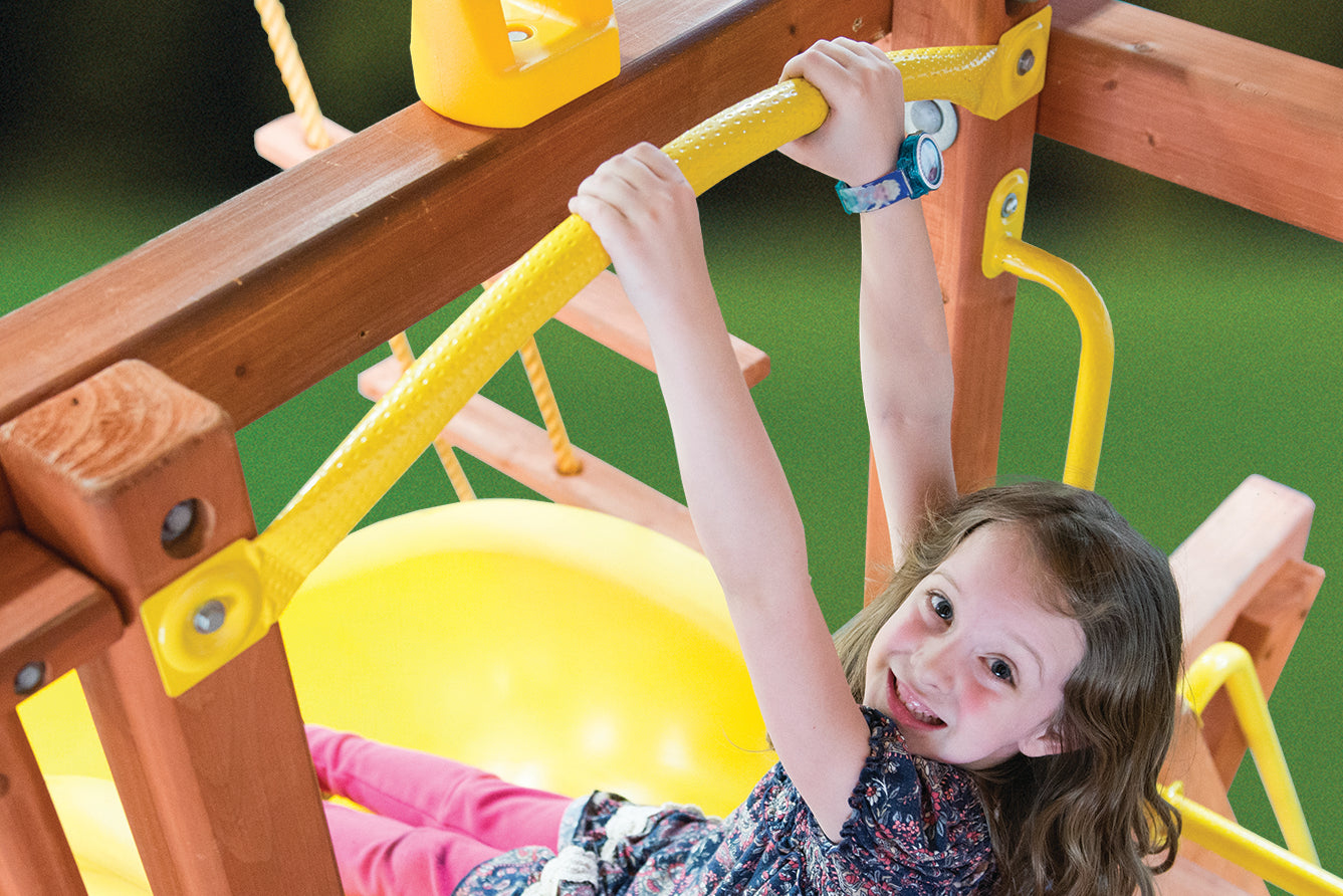 Girl playing on yellow Launch Bar playground accessory; fun, active play for kids.