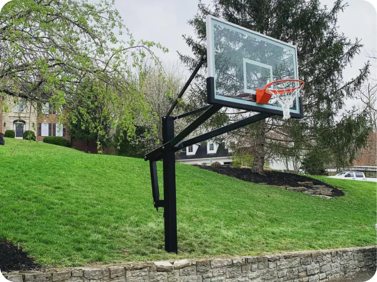In-ground basketball hoop with a glass backboard and orange rim on a grassy backyard slope